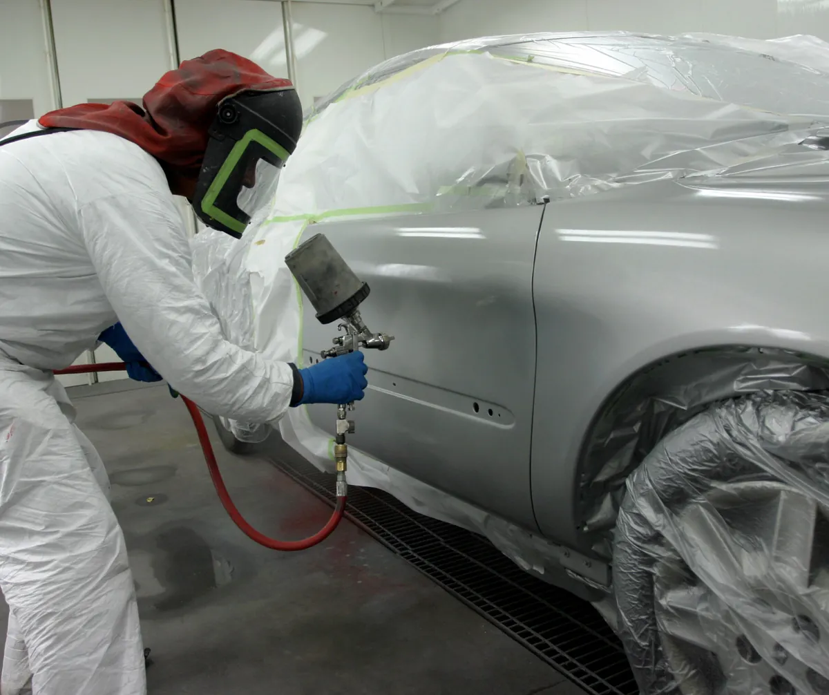 Technician applying automotive paint in a controlled booth